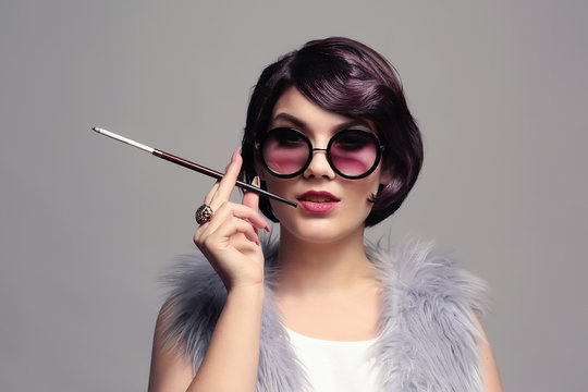 Young woman smoking with cigarette holder on grey background