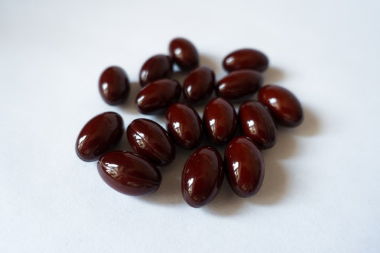Close-up of handful of dark red lutein capsules on white background