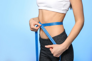 Diet concept. Young woman with measuring tape on light background