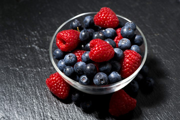 fresh berries in a glass bowl on dark background, top view