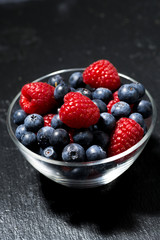 fresh berries in a glass bowl on dark background, vertical