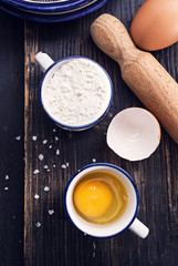 Black wooden surface with ingredients for classic pasta- egg flour salt. Free text space, top view.