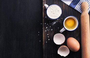 Black wooden surface with ingredients for classic pasta- egg flour salt. Free text space, top view.