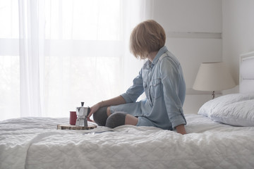Girl drinking morning coffee on a white bed reading tablet in high stockings