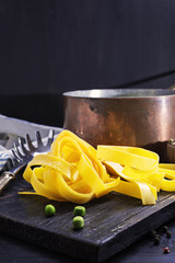 Fresh italian pasta pappardelle with green peas on old black wooden board . Selective focus, copy space, close up.