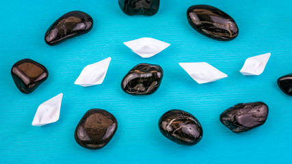 White paper boats in sigle file between abstract rock stones on blue background