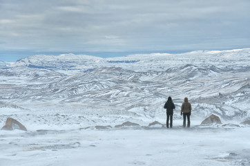 Two girls standing on the top of the hill and together watching to the rough nature of winter Iceland