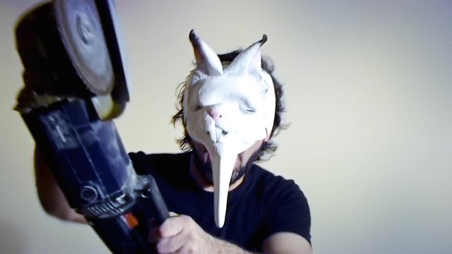 An evil man (a crazy maniac, a psycho killer) wearing a scary bunny mask runs towards us with a chainsaw. Funny comedic horror halloween shot.

