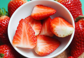 Fresh red strawberry cut in half in small white bowl.