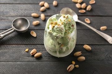 Glass with delicious melting pistachio ice-cream on black wooden background