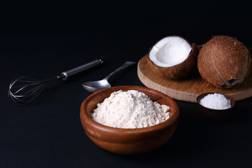 Coconut flour in wooden bowl on dark background