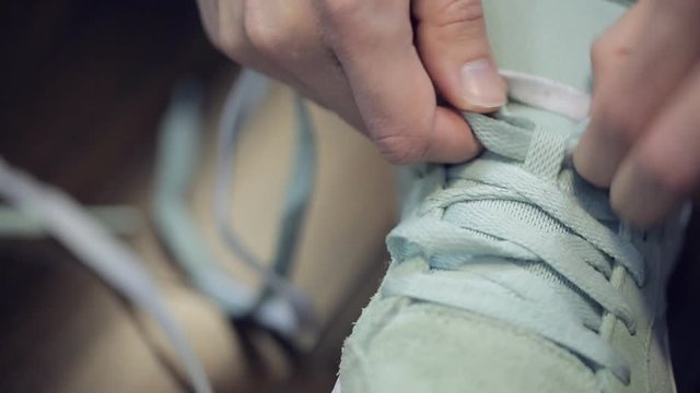 Somebody hands without manicure laces grey sneakers. On video there is right trainer with long shoelace same color with classic cross lacing. Clear arms with shot nails, stumpy fingers tighten lace