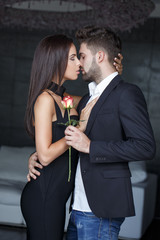 Young stylish couple kissing indoor, man give rose to woman