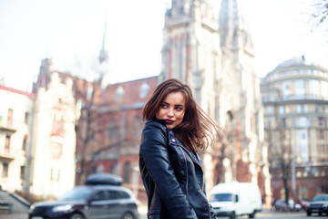 Fototapeta na wymiar young beautiful brunette walking the city.leather jacket,urban backpack , bright red lips The concept of street fashion.