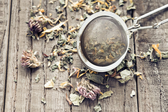 Teebl&auml;tter mit einem Teesieb auf einem Holzbrett