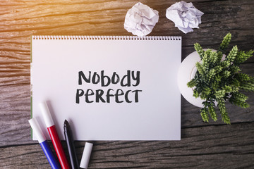 Nobody Perfect word with Notepad and green plant on wooden background.
