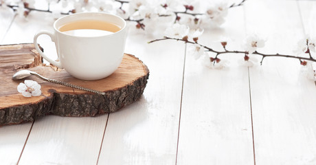 Tasse blanche de thé chaud avec des fleurs de ressort sur un fond en bois clair