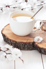 White cup of hot tea with spring flowers on a light wooden background