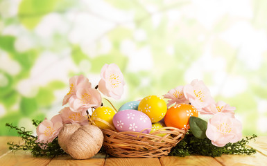 Are different Easter eggs in basket and near, grass, flowers .