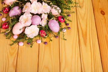 Colored easter eggs, candy, flowers, ribbon against backdrop pale wood.