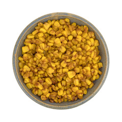 Top view of barbecue seasoned corn in an old stoneware bowl isolated on a white background.