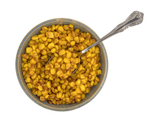 Top view of a bowl of barbecue seasoned corn with a spoon isolated on a white background.