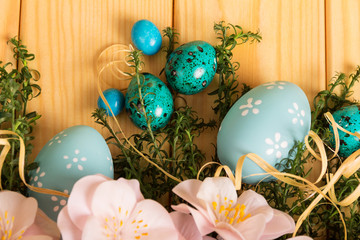 Fototapeta na wymiar Easter eggs, dragees, flowers, herbs, ribbon against backdrop pale wood.