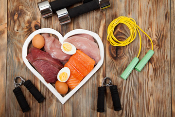 Proteins and dumbbells. Fish, cheese, eggs, meat, chicken  heart on wooden background