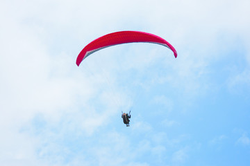 One paraglider in the blue sky with red parachute gliding for fun and excitement towards the ground.