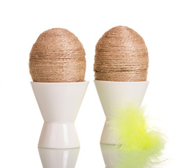 Easter eggs in cups with string entwined and feather isolated.