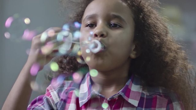 Closeup of beautiful little African girl blowing soap bubbles and smiling