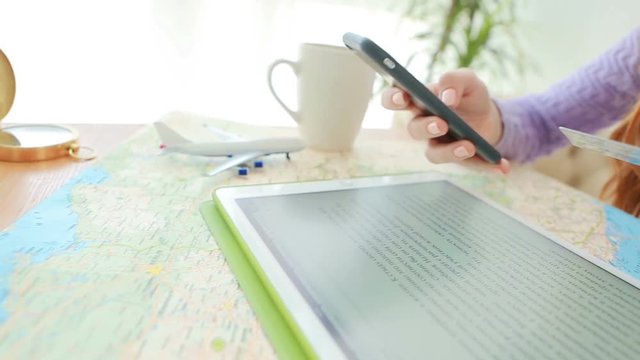 Woman sitting on the table with map, plane, compass, tablet  and Entering card details. Online payment. Video footage. Camera moving clother and Farther from the object