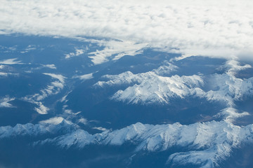 Obraz premium Idyllic snowy mountain peaks under clouds from plane