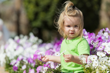 Cute happy baby boy playing at flowerbed with blossoming flowers - Powered by Adobe