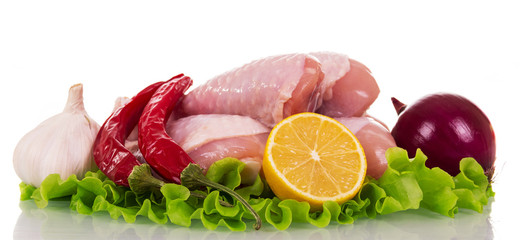 Raw chicken legs, onion, hot pepper, garlic, part of lemon and lettuce leaves isolated on white.