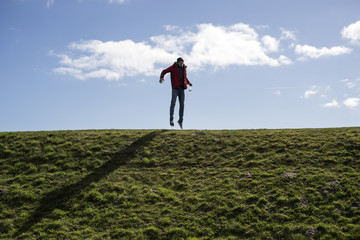 Mann auf einem Deich springt und macht faxen vor blauem Himmel