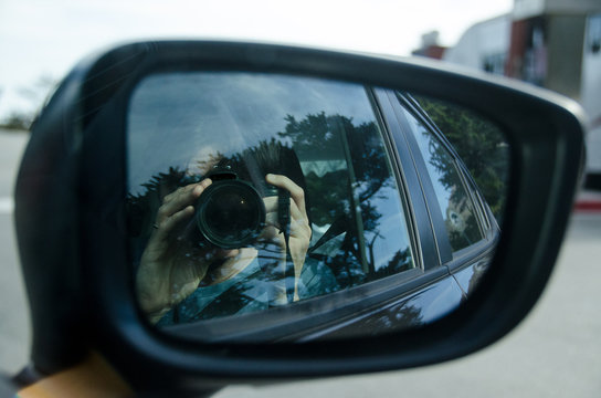 Person reflected in car side mirror taking photos out of window