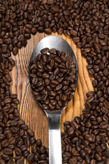 Aromatic goodness. A spoon full of roasted coffee beans surrounded by coffee beans scattered on the table...