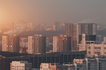 Close-up shooting from top of morning metropolitan city with grey unfinished residential or office building under construction with, scaffolding surrounded by multiple houses of residential district