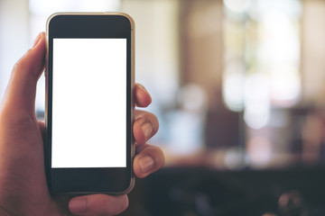 Mockup image of hand holding black mobile phone with blank white screen in vintage wooden cafe and blur bokeh background