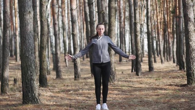 Young woman doing fitness exercises outdoors. Fit girl doing Jumping and running on the spot in park. Workout and fitness in forest. Attractive woman doing stretching exercises. slow motion