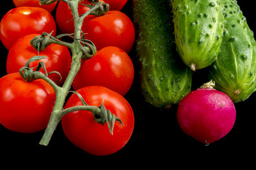 red tomatoes, green cucumbers and radish on black background
