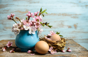 Easter background with easter eggs in nest, pink blooming flowers on old wooden table with copy space