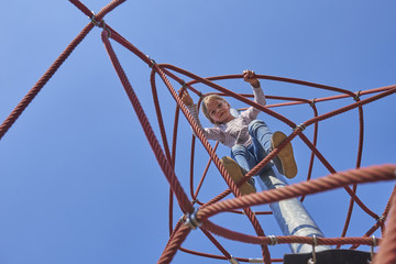 Active young child girl climbing the spider web playground activity. Children summer activities.