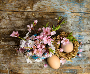 shabby chic Easter background with easter eggs in nest , blooming flowers on old wooden table. top view with copy space