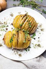 Baked potatoes with thyme on a plate, herbs, pepper closeup on a gray background.