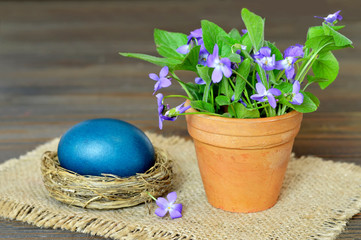 Easter card with blue Easter egg in the nest and violet flowers