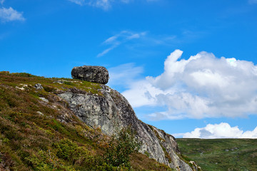 Fototapeta na wymiar Big granite boulder lying on the outmost edge of a Mountain crag in a summer landscape in Telemark, Norway