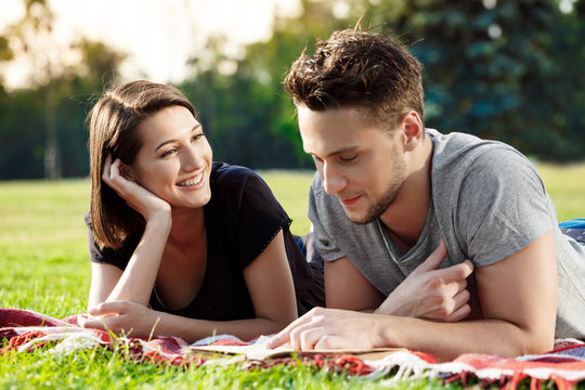 Young beautiful couple smiling, reading, resting on picnic in park.