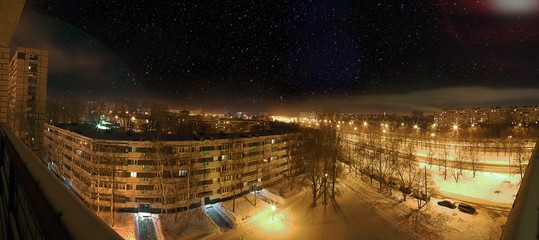 Panorama of night city under falling snow